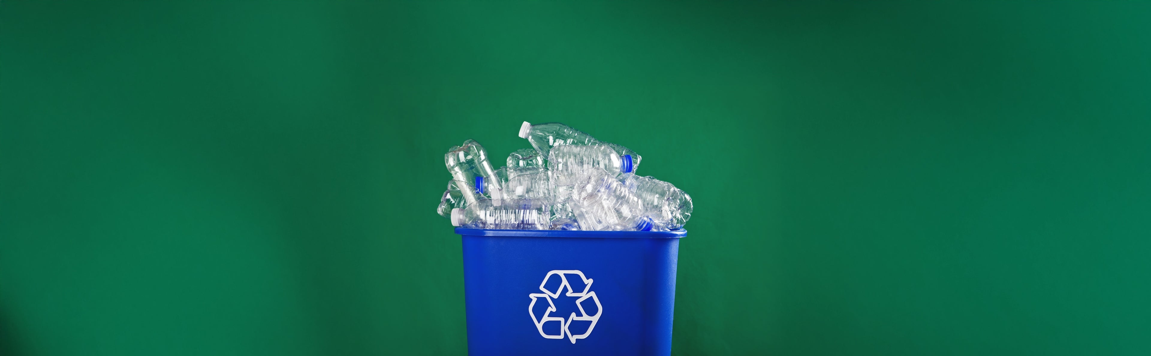 Blue recycling bin with plastic bottles against a green background